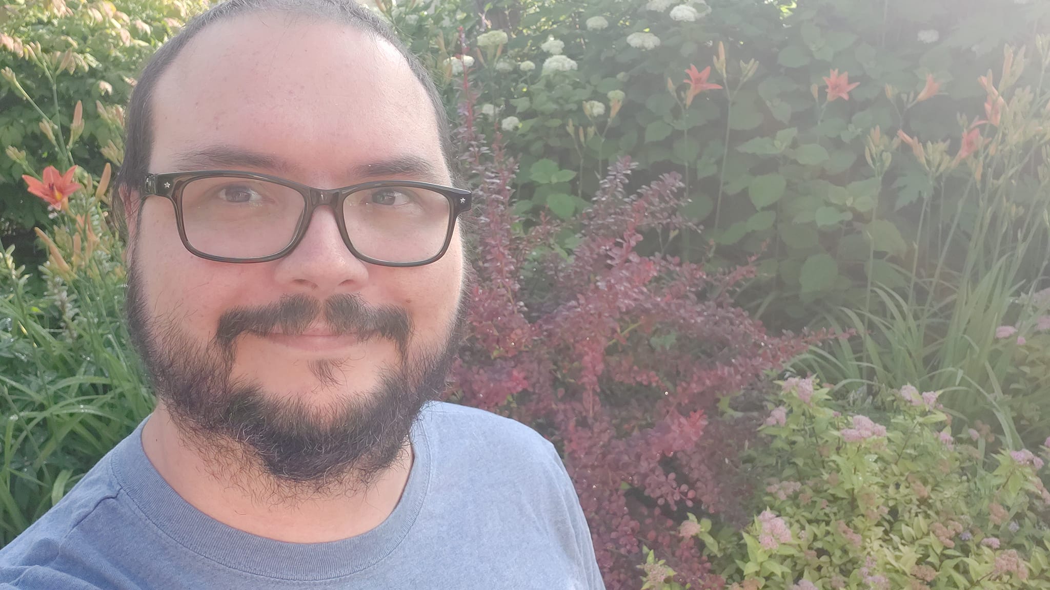 A man is dressed in a t-shirt standing in front of a flower garden